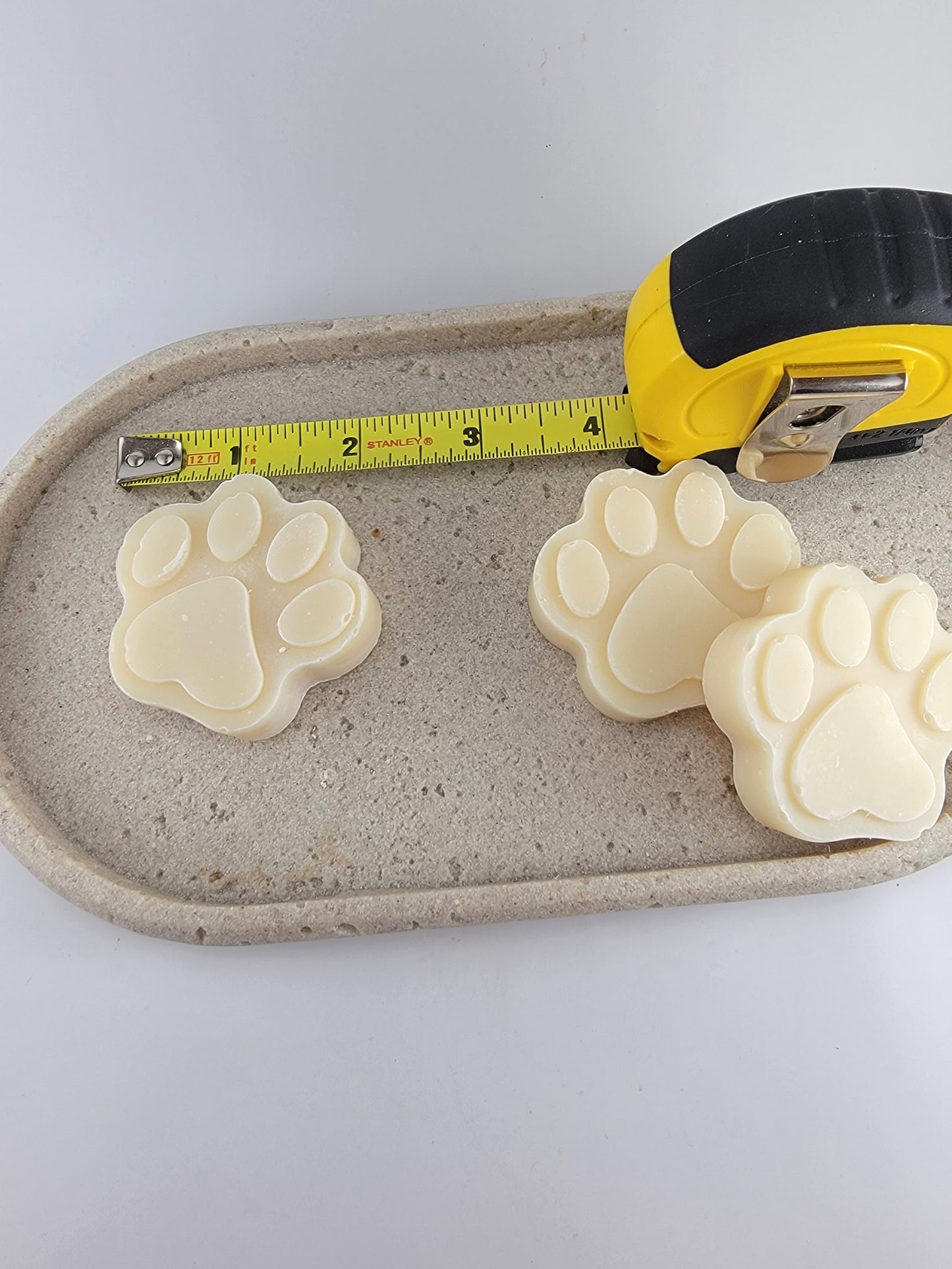 Two paw-shaped bars of dog shampoo with ruler on marble surface.