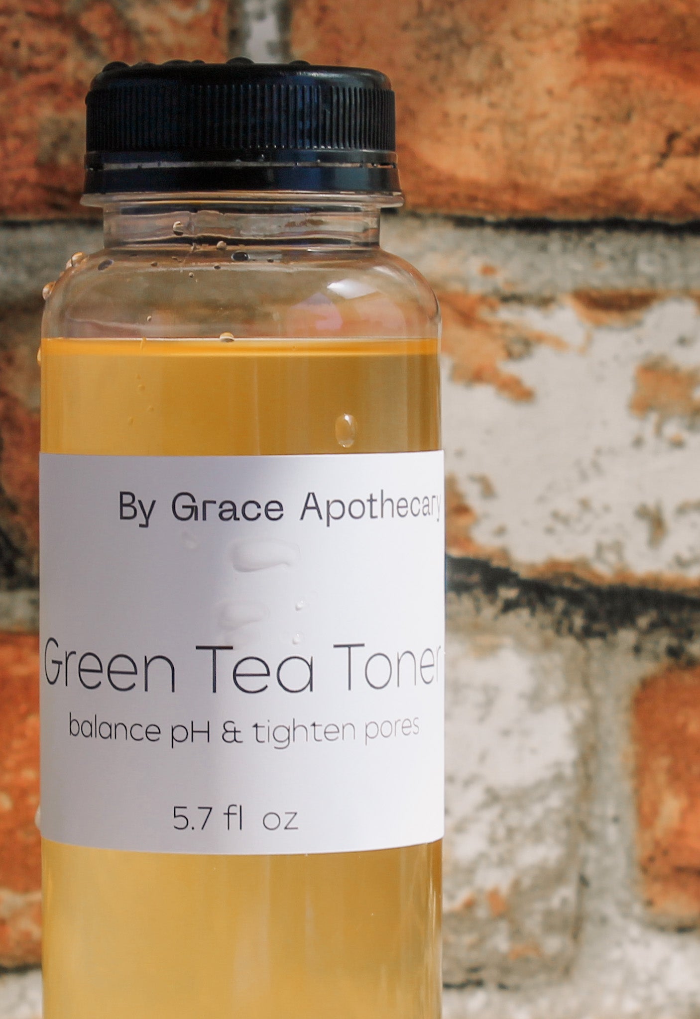 Bottle of Green Tea Toner by Grace Apothecary against a textured brick wall background