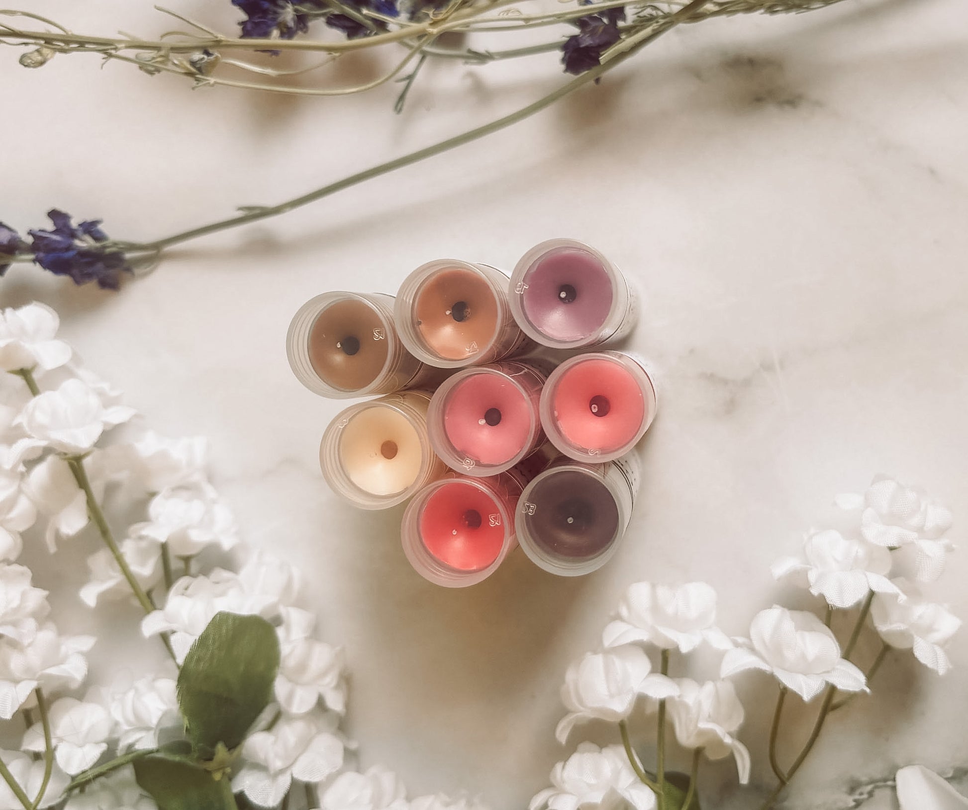 Set of lip gloss tubes on a marble surface with flowers around