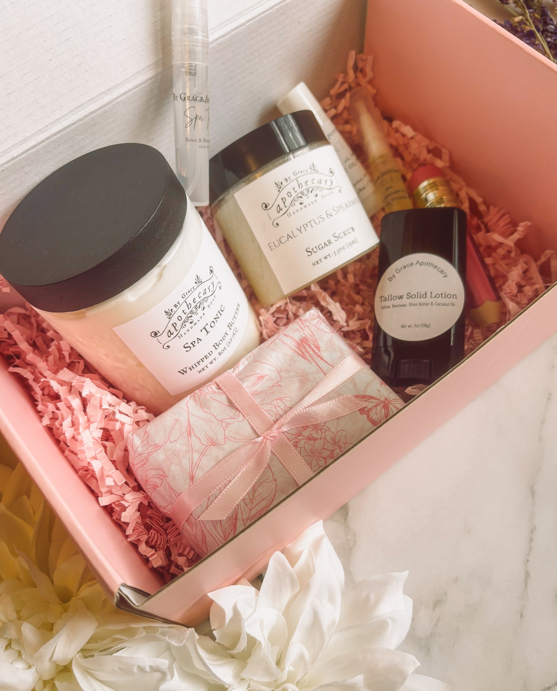8 products in pink gift box on marble counter.