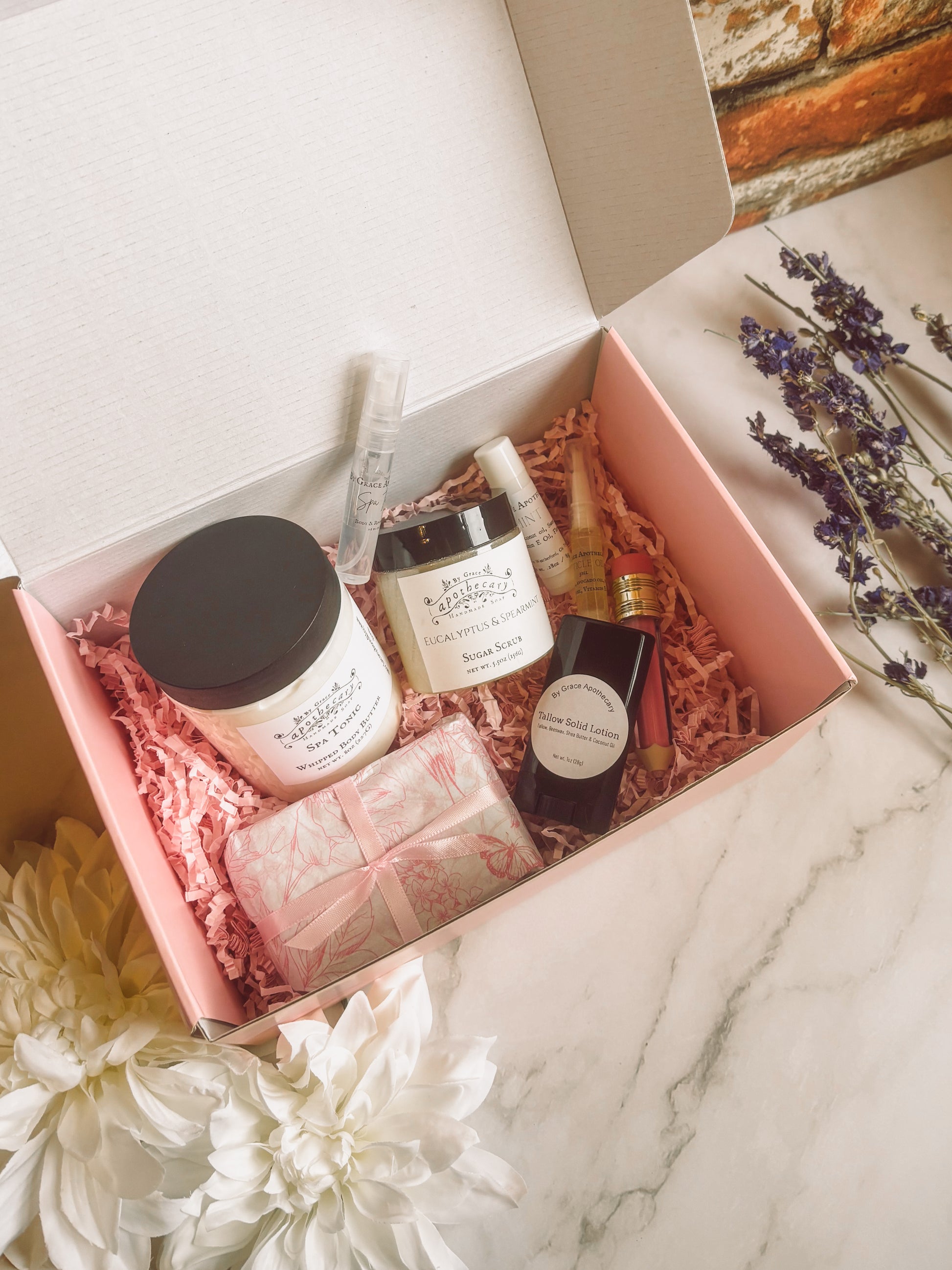 8 products in pink gift box on marble counter.