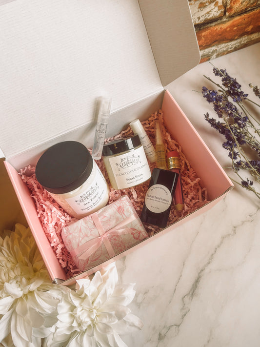 8 products in pink gift box on marble counter.