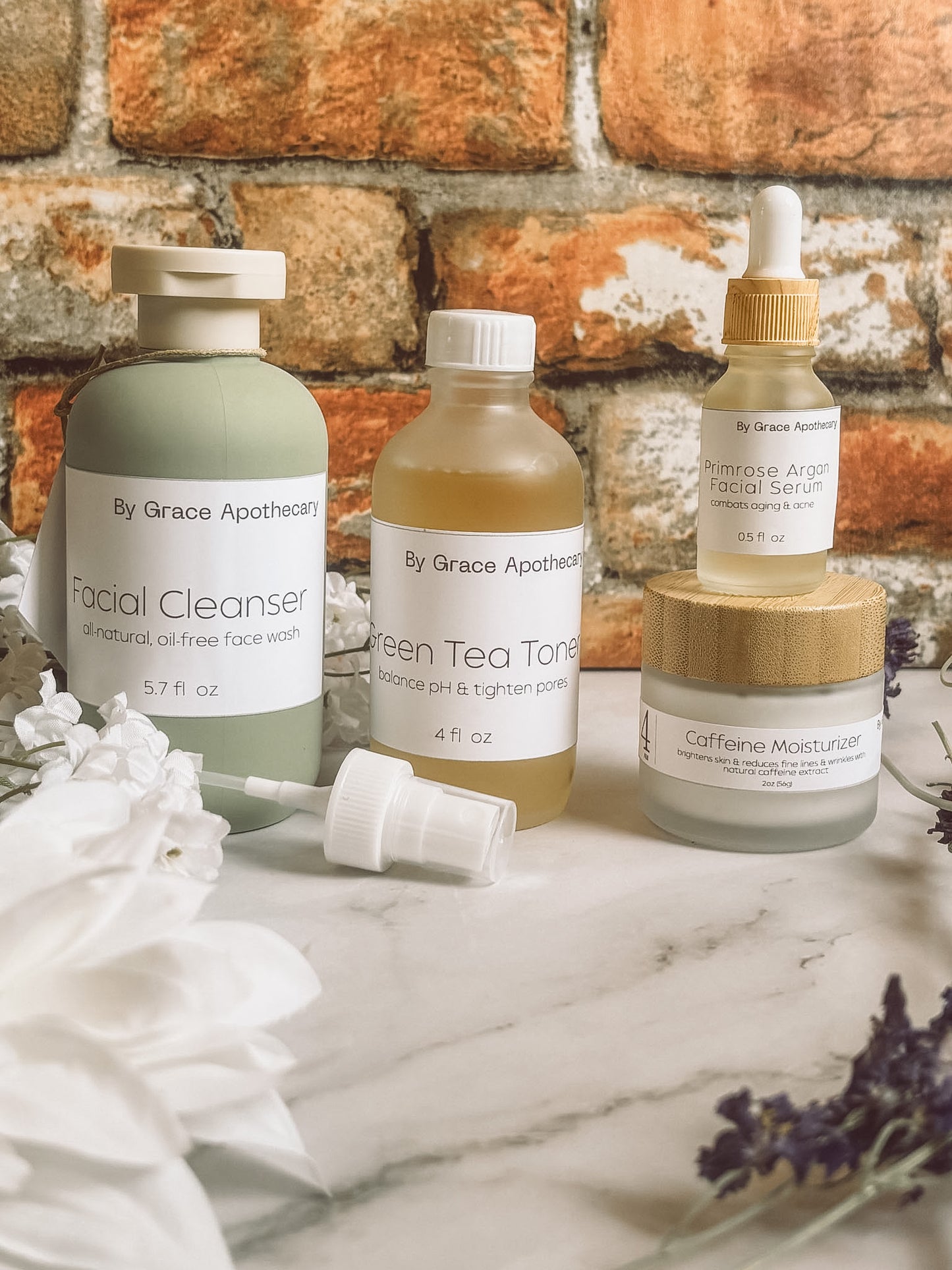 4 skin care products on a marble counter with brick background and flowers.