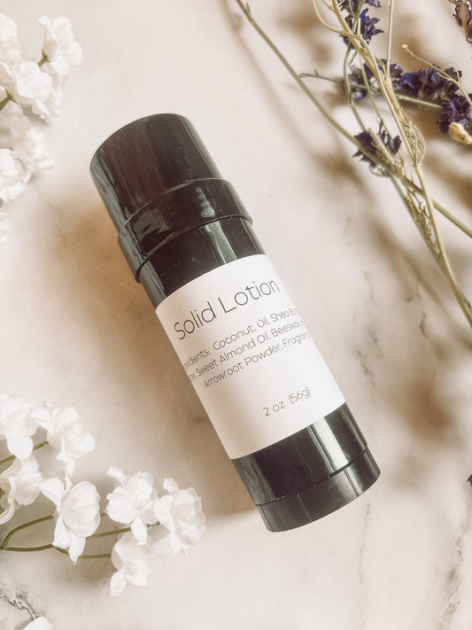 Solid lotion bar with black container and white label on a light background with flowers.